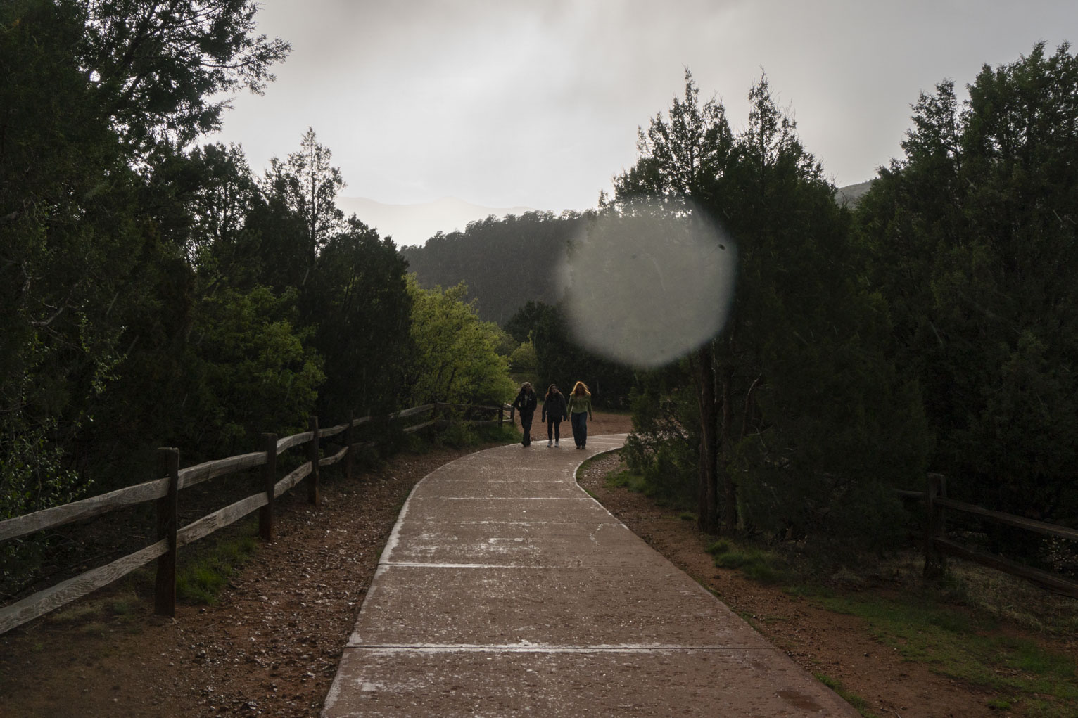 Three people walk down a path after rain